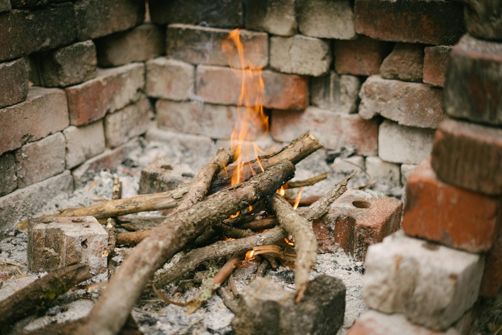 A small campfire flickering within a rustic brick enclosure outdoors.