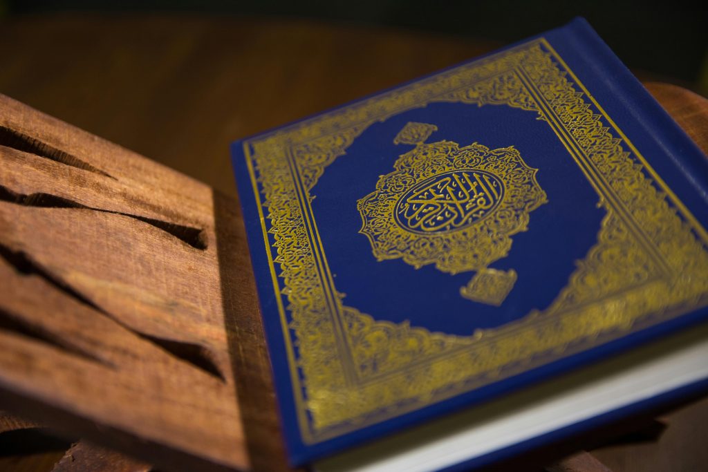Close-up of a Quran with intricate gold calligraphy resting on a carved wooden stand.